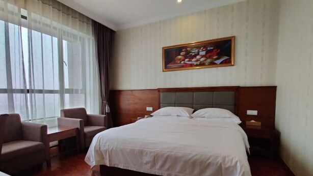 A hotel room with a bed, two chairs, a table, a painting on the wall, and a window with curtains. - Vienna Classic Hotel (Shanghai)