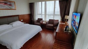 A hotel room with a bed, two armchairs, a desk with a lamp, a television, and a large window with curtains. - Vienna Classic Hotel (Shanghai Tinglin) (Shanghai)