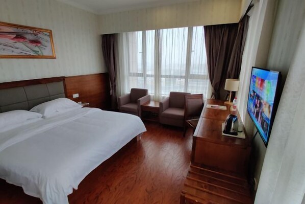 A hotel room with a bed, two armchairs, a desk with a lamp, a television, and a large window with curtains. - Vienna Classic Hotel (Shanghai)