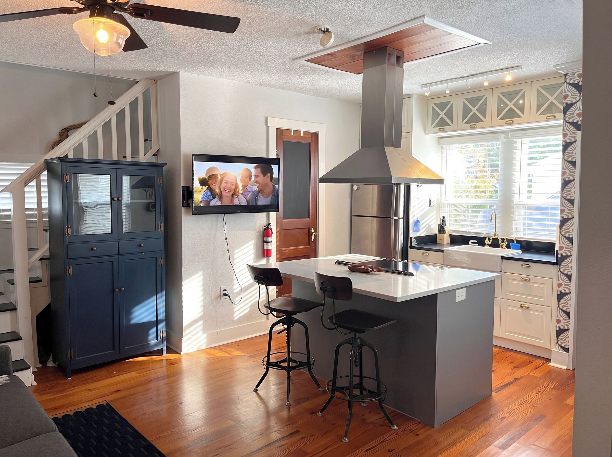A modern kitchen with a central island, bar stools, a built-in oven, and a television mounted on the wall.