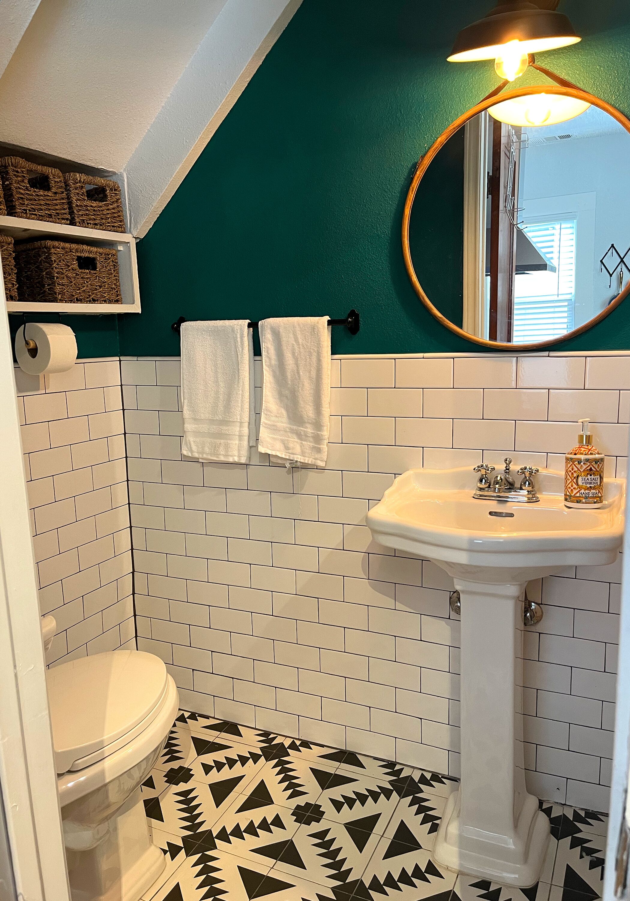 A bathroom with white subway tiles, a black and white patterned floor, a white sink with a mirror above it, and two white towels hanging on a rack.