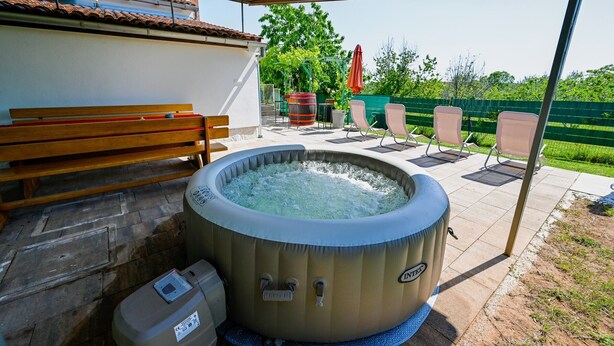An outdoor hot tub area with a wooden bench, outdoor chairs, and a covered patio.