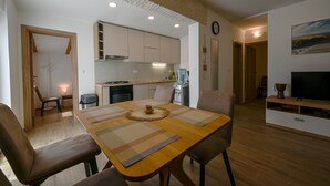 A modern kitchen with wooden cabinets, a dining area with a wooden table and chairs, and a living area with a TV and entertainment unit.