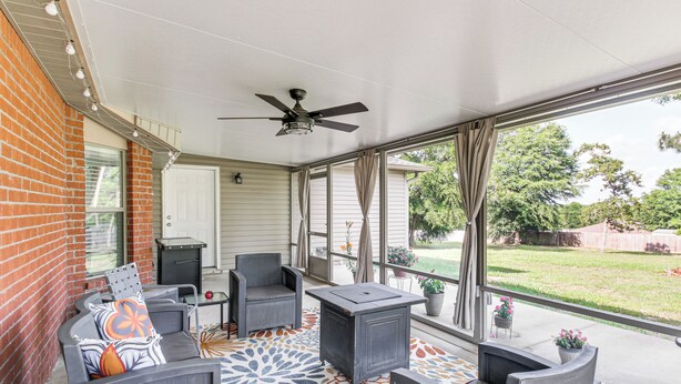 Eine überdachte Terrasse mit Deckenventilator, grauer Gartenmöbel und einem gemusterten Boden.