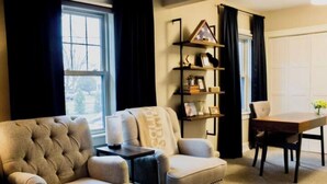 A living room with a tufted armchair, a sofa, a small table, and a bookshelf.