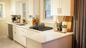 A modern kitchen with white cabinetry, a built-in stove, and a window with curtains.