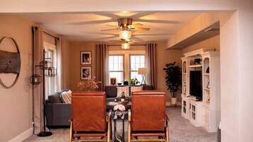 A dining area with a table and chairs, a ceiling fan, and a sofa in the background.