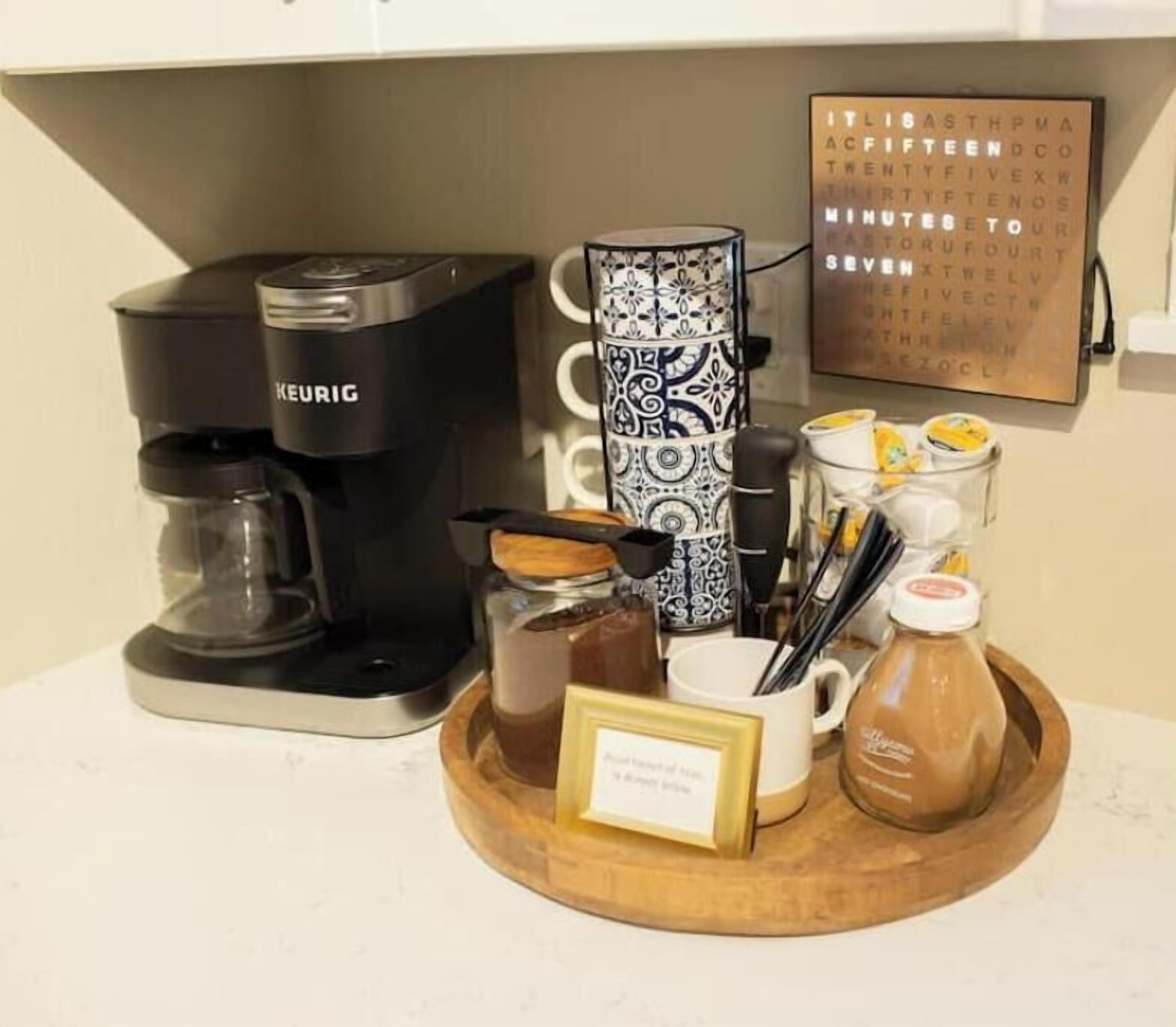 A coffee station with a Keurig coffee maker, a tray with coffee mugs, a jar of sugar, and a sign indicating the coffee is freshly made.