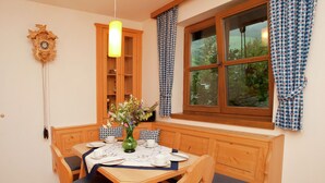 A dining area with a wooden table set for four, blue cushions, a vase with flowers, a wooden cabinet, and a window with checkered curtains. - Flat in Mittersill Near Ski Slopes (Mittersill)