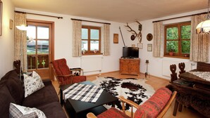 A cozy living room with a brown sofa, a wooden coffee table, and a red armchair. There are two windows with curtains, a television, and a fireplace. - Flat in Mittersill Near Ski Slopes (Mittersill)