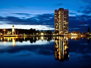 A high-rise building with a modern design, situated by a calm body of water reflecting the building and surrounding lights. - Apartment in Lubeck-travemunde (Lübeck)