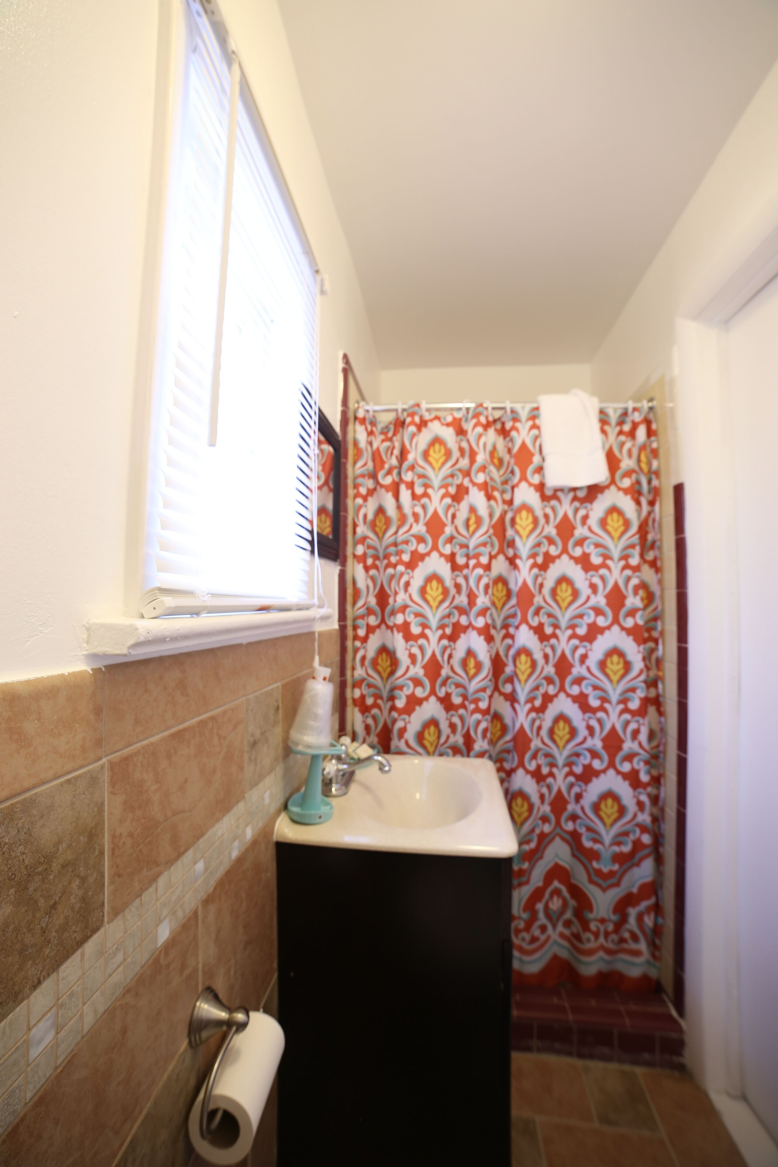 Un baño con ventana, lavabo, dispensador de papel higiénico y cortina de ducha.