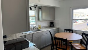 A kitchen with grey cabinets, a granite countertop, a coffee maker, and a window with a view of the street. - El Ray motel (Wildwood)