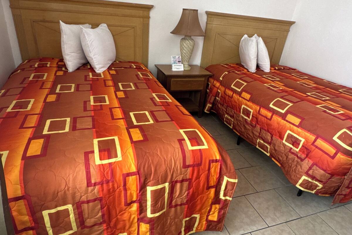 Two single beds with wooden headboards, a nightstand with a lamp, and a patterned bedspread.