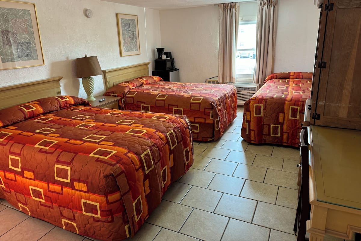 A hotel room with two beds, a desk, a lamp, a coffee maker, and a wardrobe.