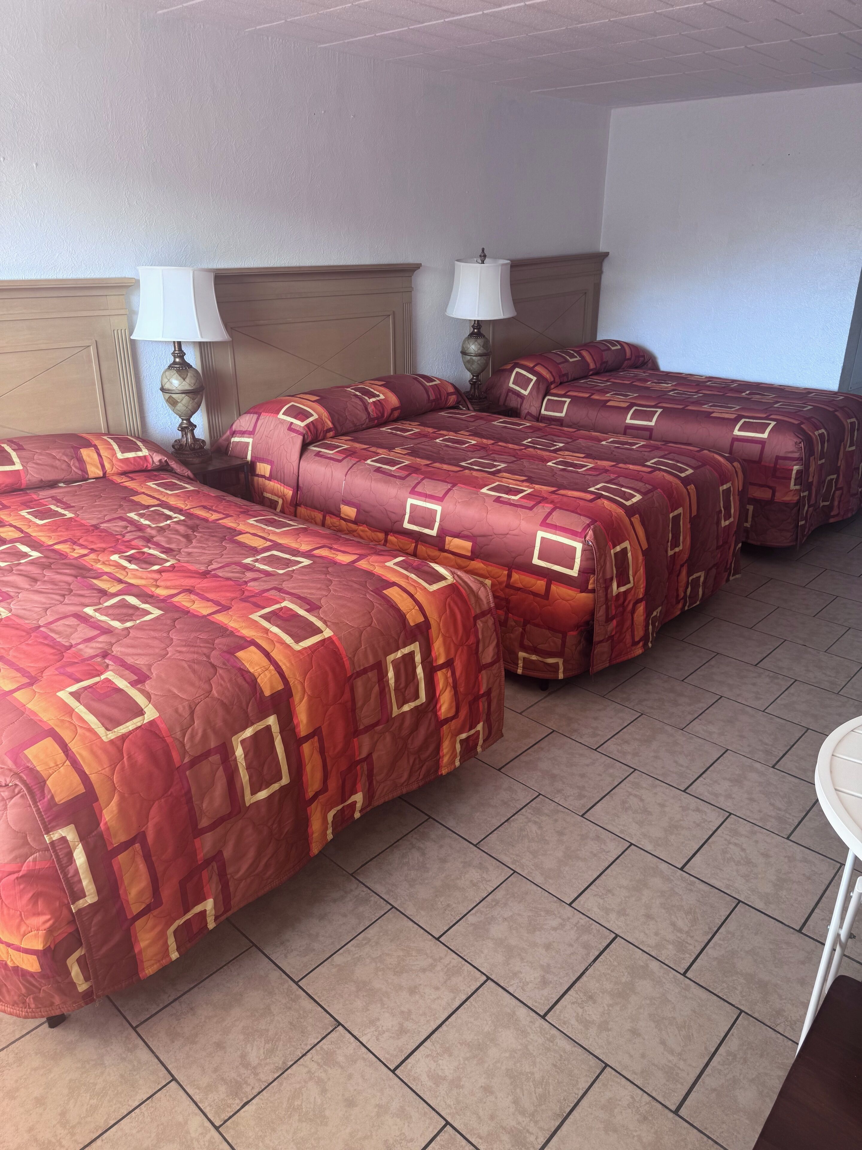 Ett hotellrum med fyra sängar, var och en med ett mönstrat överkast, två sänglampor och en sänggavel i trä.