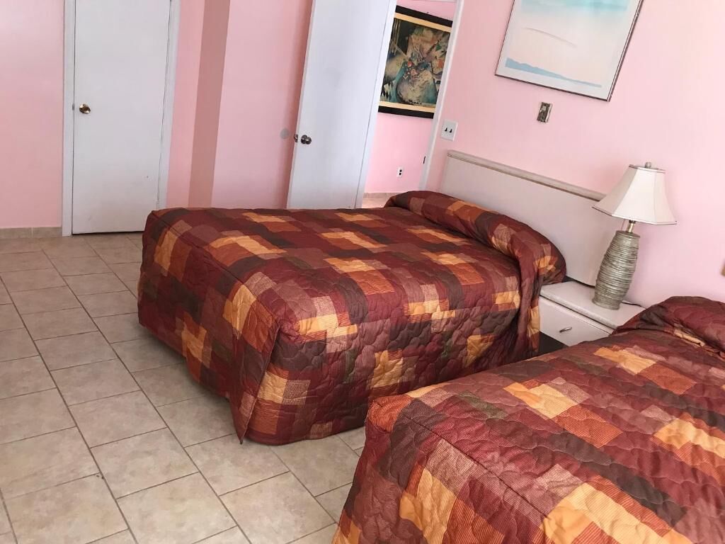Une chambre avec deux lits, une table de chevet avec une lampe et une porte.