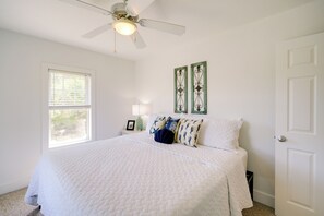 A bedroom with a bed, a ceiling fan, a window, and two wall decorations. - Buxton Vacation Rental w/ Shared Canal Access! (Buxton)