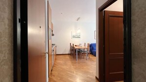 A hallway leading to a dining area with a wooden table and chairs, a blue sofa, and a painting on the wall. - La Piazzetta Verde - Affitti Brevi Italia (Lecco)