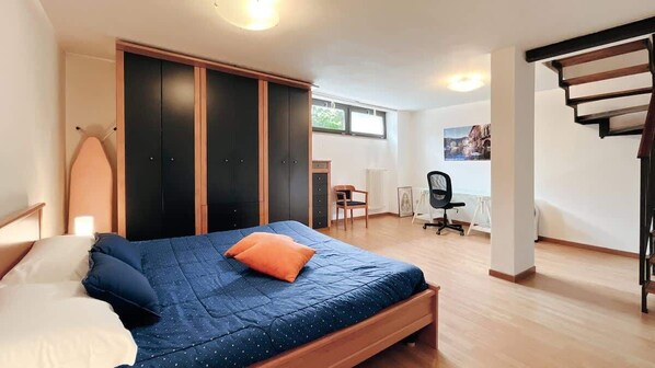 A bedroom with a bed, a desk, and a chair. There is a window and a door.