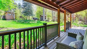 Une véranda abritée donnant sur un jardin bien entretenu, comprenant une pelouse, des arbres et un petit abri de jardin.