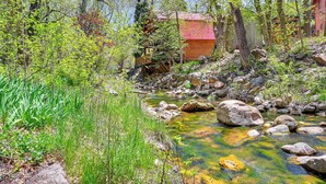 Un chalet rustique avec un toit rouge, entouré d’un ruisseau rocheux et d’une végétation luxuriante.