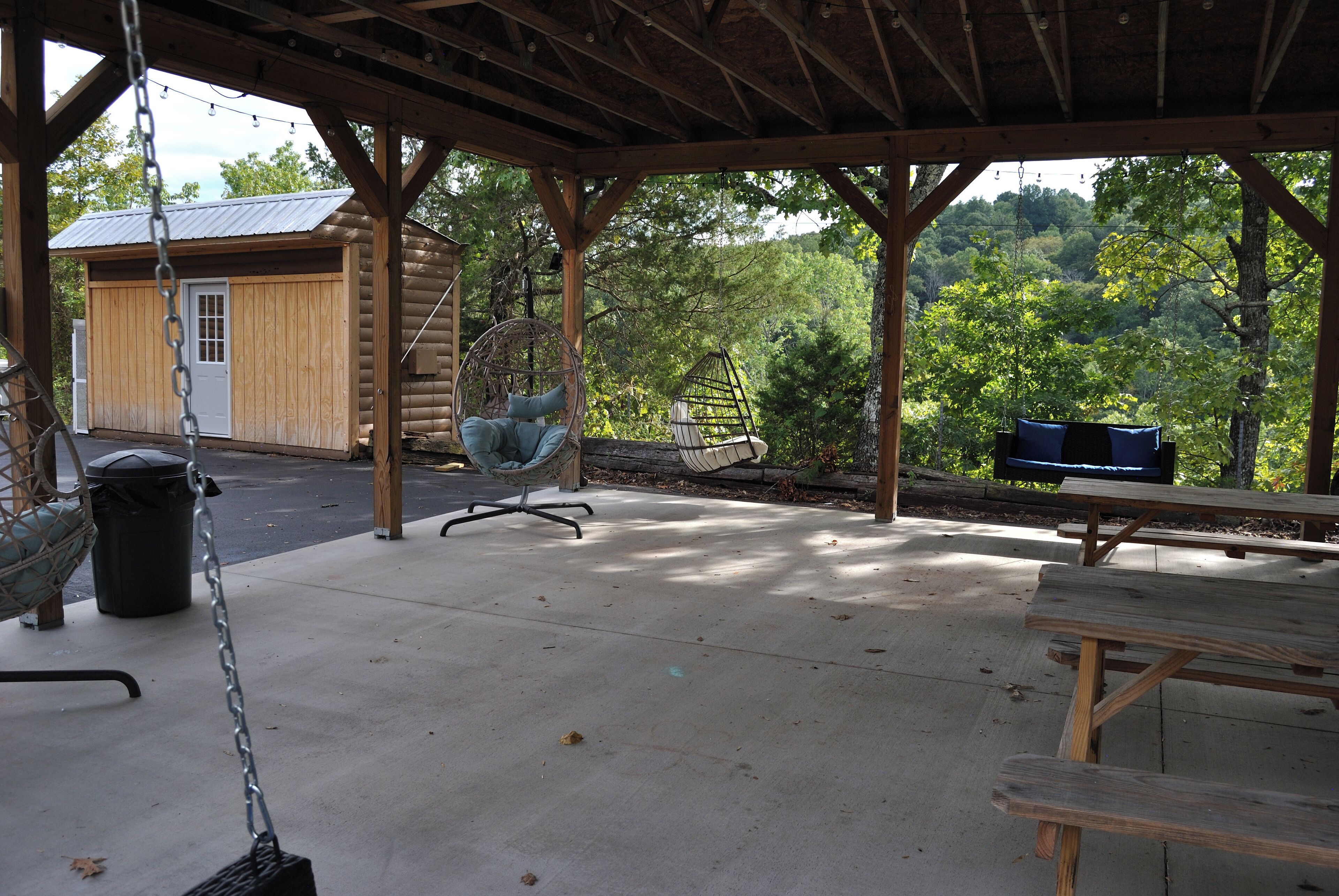 A covered outdoor area with a swing chair, a hanging chair, and a picnic table.