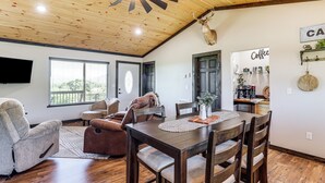 A spacious living room with a wooden ceiling, a dining area with a wooden table and chairs, a mounted deer head, and a coffee station. - Arkansas Retreat w/ Deck, Fire Pit & Mtn Views! (Jasper)