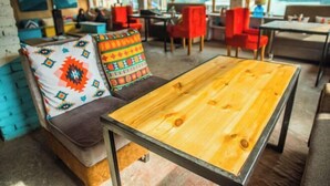 A cozy interior with a wooden table, colorful pillows, and red chairs. - Young Monk Hostel & Cafe Old Manali (Manali)
