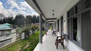 A covered outdoor area with a row of windows and a few chairs. - Young Monk Hostel & Cafe Old Manali (Manali)