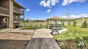 Een gebouw met twee verdiepingen, een balkon, een houten terras en een prieel in een gazon.