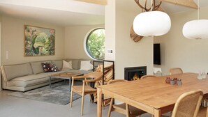 A modern living room with a wooden dining table, rattan chairs, a sofa, and a fireplace. - 10 Person Holiday Home in Vejby (Vejby)