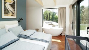 A bedroom with a large bed, a bathtub, and a view of a garden. - 10 Person Holiday Home in Vejby (Vejby)