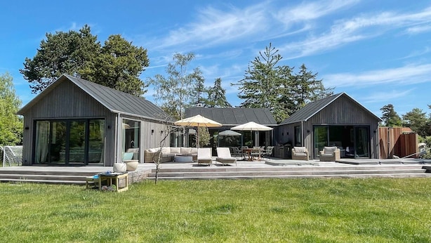A modern house with large glass windows, a covered patio with outdoor furniture, and a well-maintained lawn. - 10 Person Holiday Home in Vejby (Vejby)