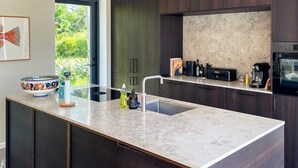 A modern kitchen with dark wooden cabinets, a large island with a sink, and a built-in oven. - 10 Person Holiday Home in Vejby (Vejby)