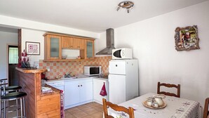 Une cuisine compacte avec des meubles en bois, un four à micro-ondes et un réfrigérateur. On y trouve une table à manger avec des chaises et un petit îlot avec des tabourets.