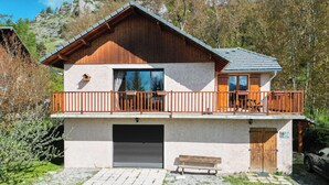Une maison en bois à deux étages, dotée d’un balcon, d’un garage et d’un banc devant l’entrée.