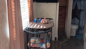 A compact room with a round table, a television mounted on the wall, and a window with curtains.