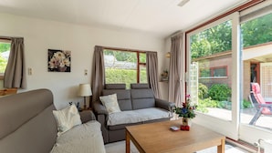 A spacious living room with two sofas, a coffee table, and large windows offering a view of the garden. - Holiday Home Zeeland Near Westerschelde (Baarland)