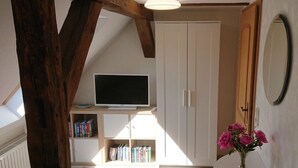 A room with a TV on a stand, bookshelves, a white wardrobe, a mirror, and a vase with flowers. - Holiday Apartment Red Milan (Bobitz)