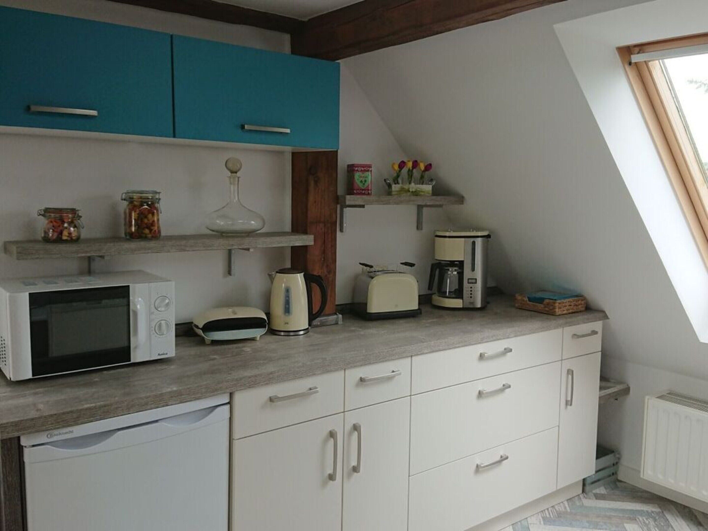 Cucina con mobili bianchi, forno a microonde, bollitore, tostapane e macchina da caffè. Si vede il cielo da una finestra.