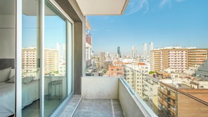 Ein Balkon mit Blick auf die Stadt, ein Bett und ein Sessel.