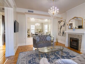A spacious living room with a grey sofa, a glass coffee table, and a chandelier. - Elegant Victorian Parlor (El Paso)