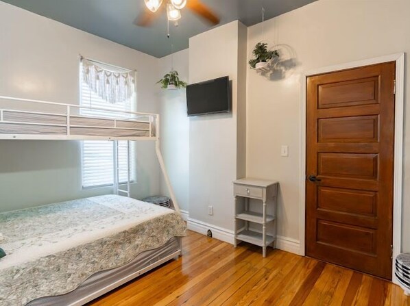 A bedroom with a bunk bed, a small desk, a TV, and a door.