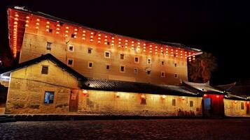 Um edifício grande com várias janelas e telhado tradicional, iluminado por luzes quentes.