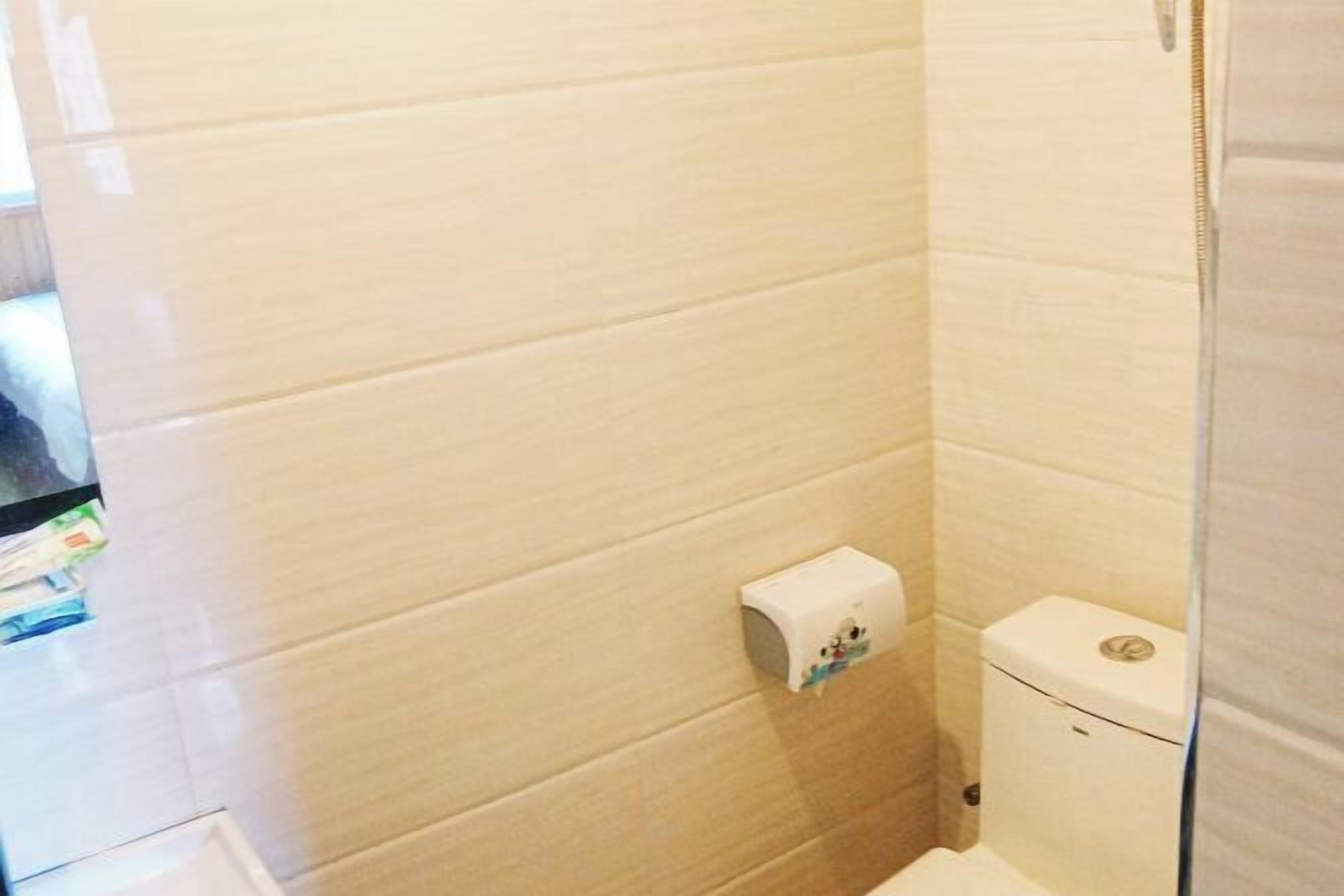 A bathroom with white tiled walls, a toilet, and a paper towel dispenser.