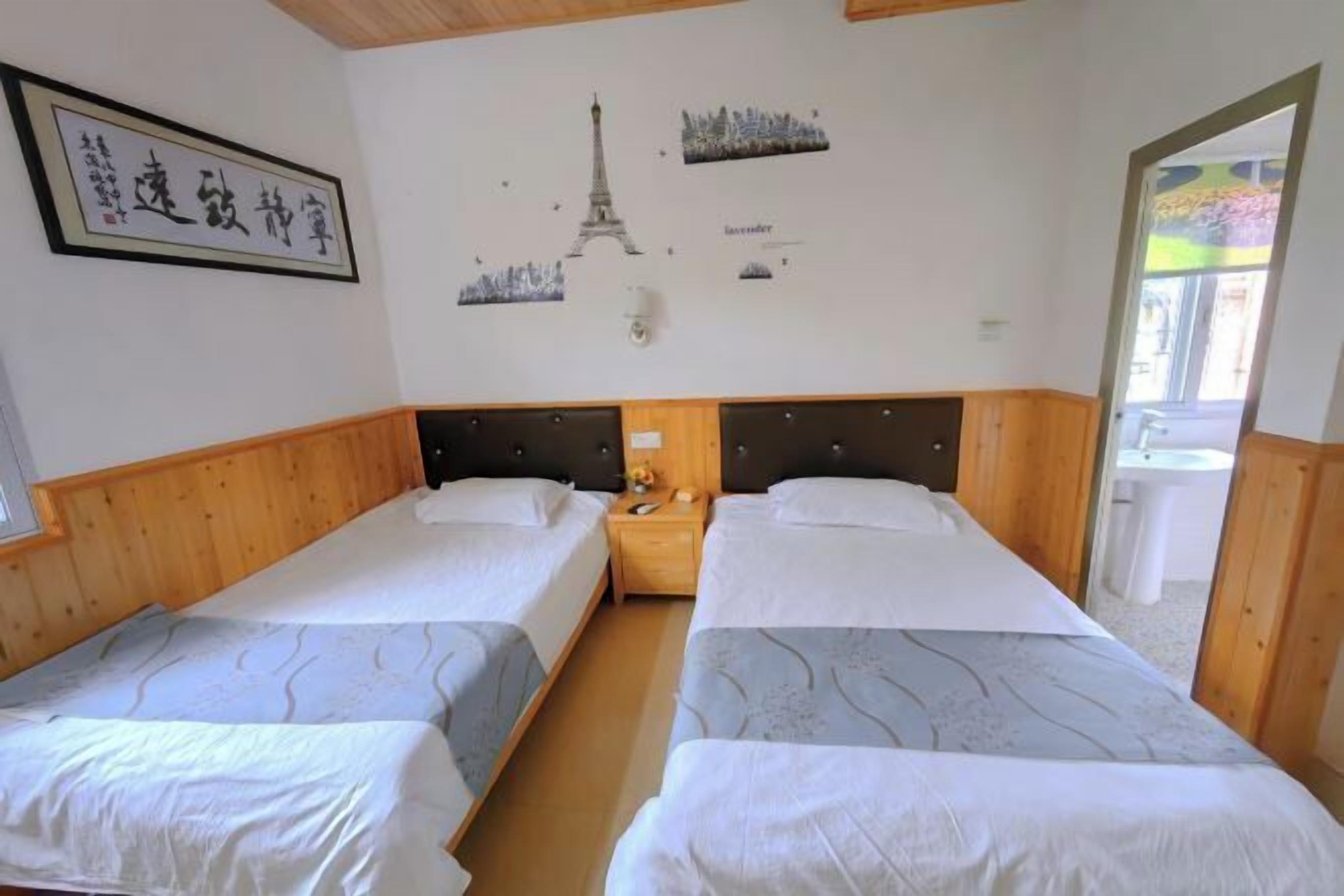 A hotel room with two single beds, wooden headboards, a nightstand with a lamp, and a wall with a cityscape and Eiffel Tower illustration.