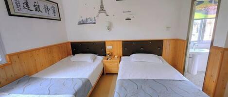 Ett hotellrum med två separata sängar, sänggavlar i trä, ett nattduksbord med en lampa och en vägg prydd med en illustration av en stadsbild och Eiffeltornet.