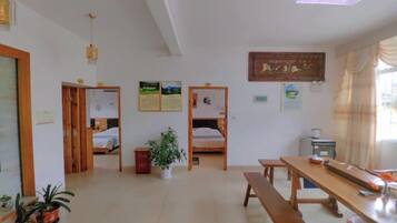 A room with a wooden bench, a table, and two beds with wooden frames.