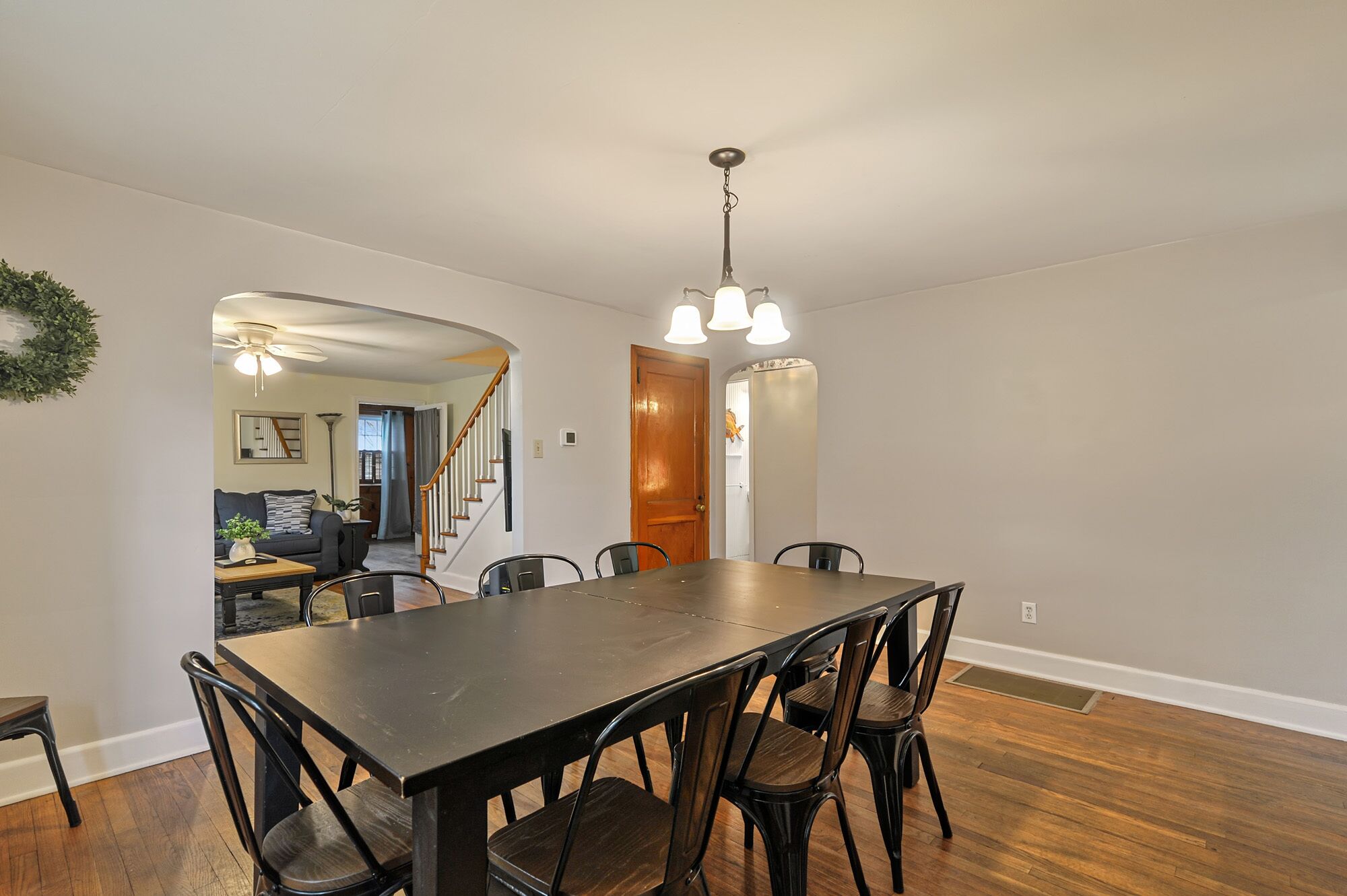 A dining area with a rectangular table and six chairs, a wooden staircase, and a hallway leading to another room.